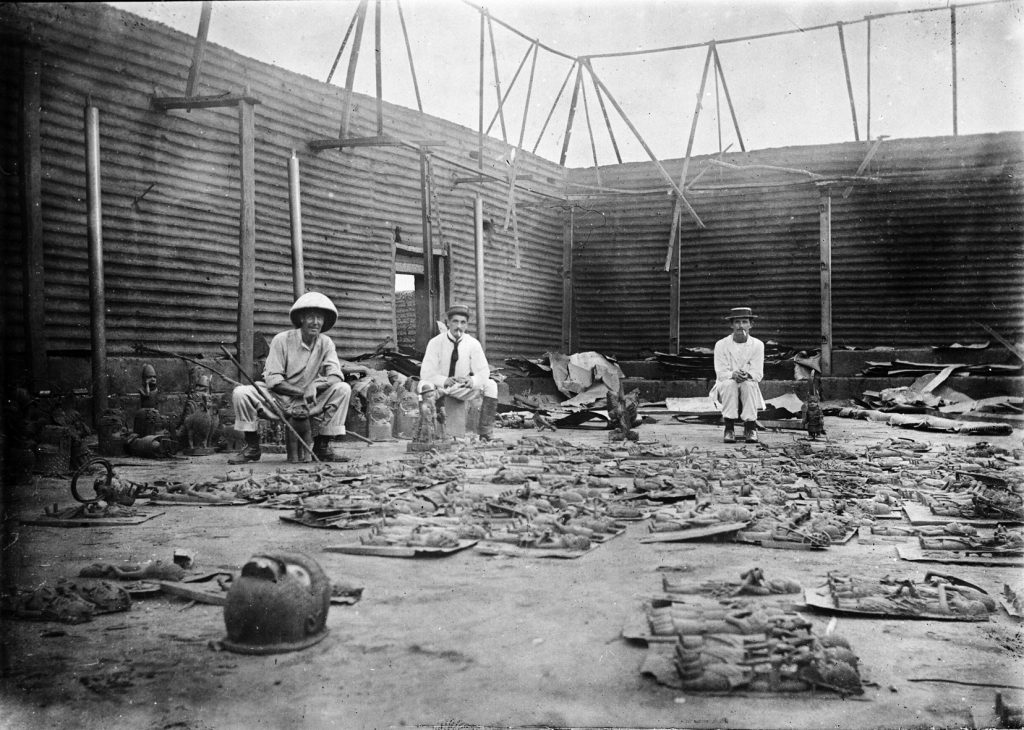 Interior of Oba's compound burnt during siege of Benin City (present day Nigeria) , with bronze plaques in the foreground and three British soldiers of the Benin Punitive Expedition 9-18 February 1897